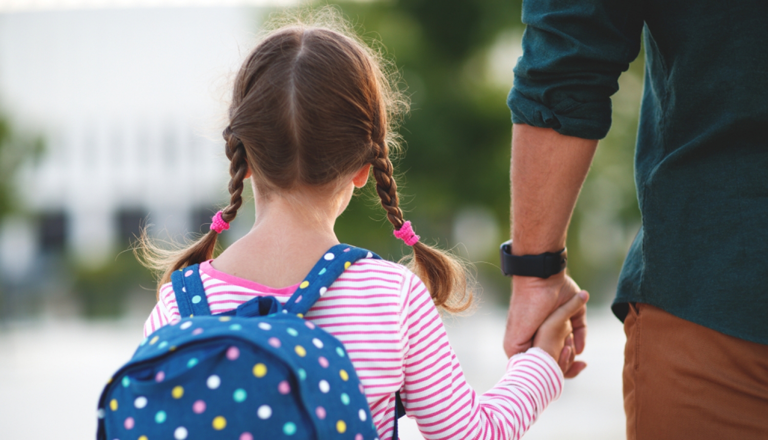 Meitenīte ar skolas somu tur roku tētim