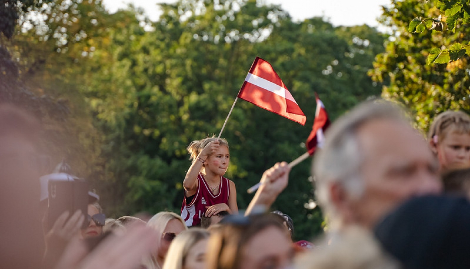 Basketbolistu sagaidīšana pie Brīvības pieminekļa. Meitene tur rokās Latvijas karogu. 