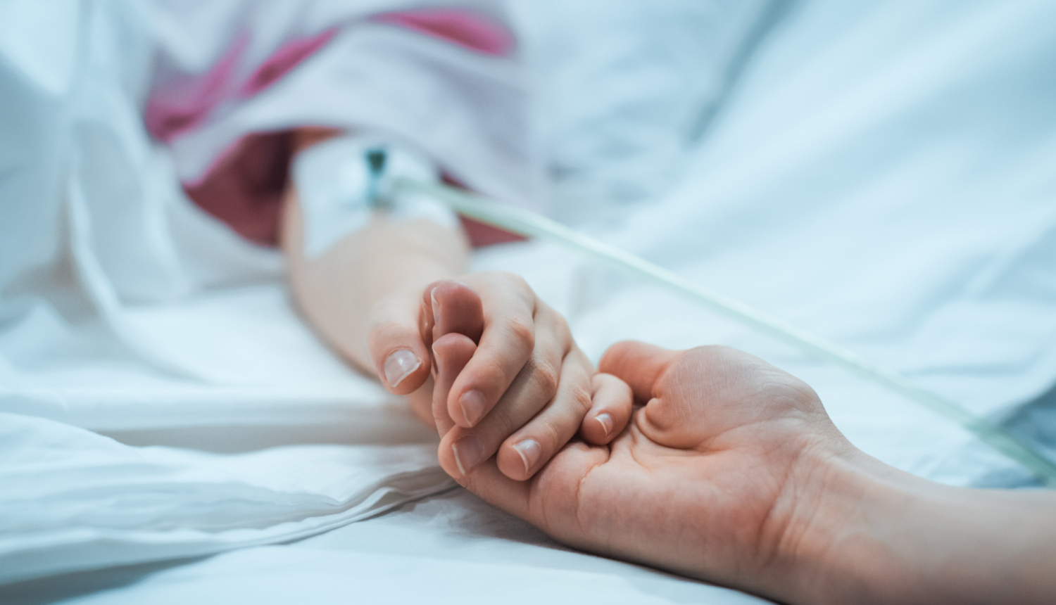 Vecāks tur slimnīcas gultā guloša bērna roku