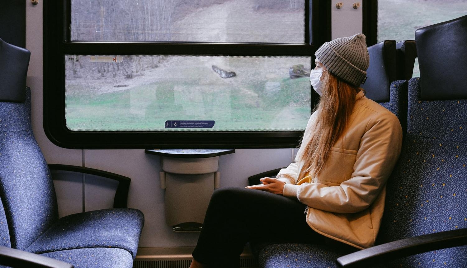 Meitene ar masku sēž vilcienā
