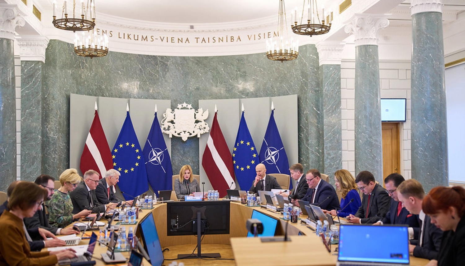 Ministri un Ministru prezidente un Valsts kancelejas direktors sēž Ministru kabineta sēžu zālē pie galda.