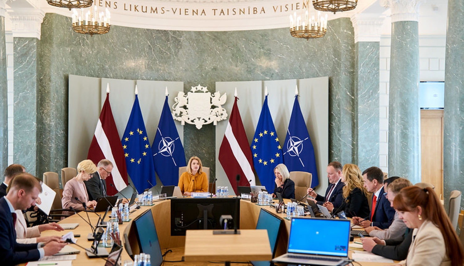 Ministru kabineta sēde. Ministru prezidente un ministri sēž pie sēžu galda. Fonā Latvijas, ES un NATO karogi un ģerbonis. 
