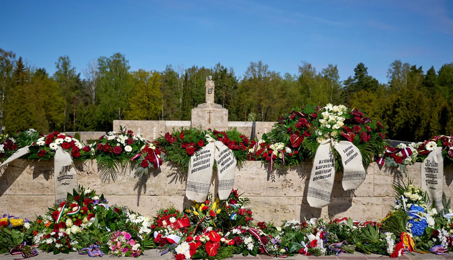 Brāļu kapu siena ar Māti Latviju. Ziedu vainagi ar lentām kritušo karavīru piemiņai. 