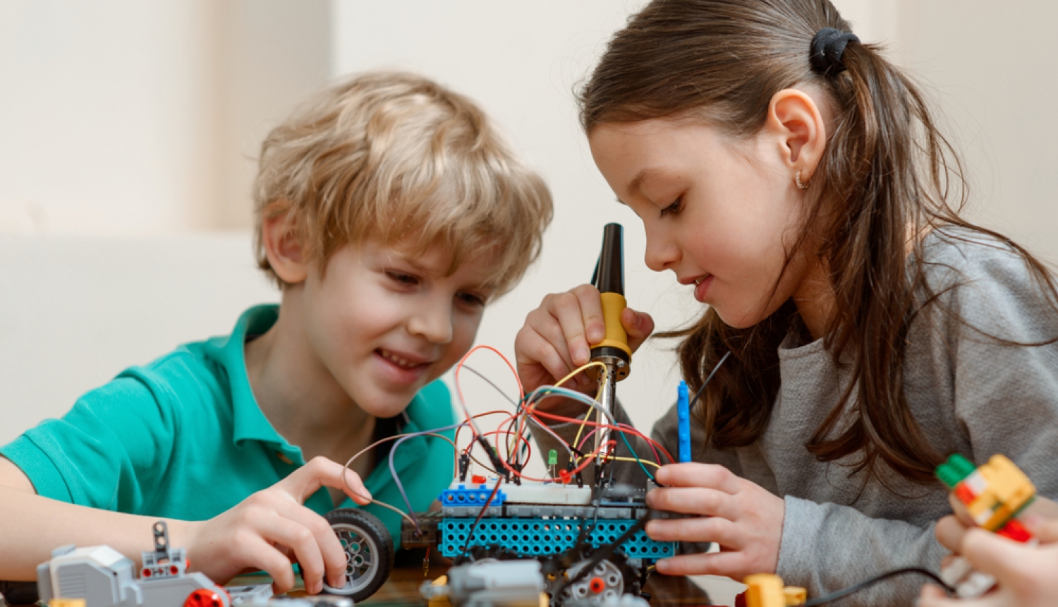 Zēns un meitene darbojas ar tehnoloģijām - būvē auto, kuram pieslēgti vadi