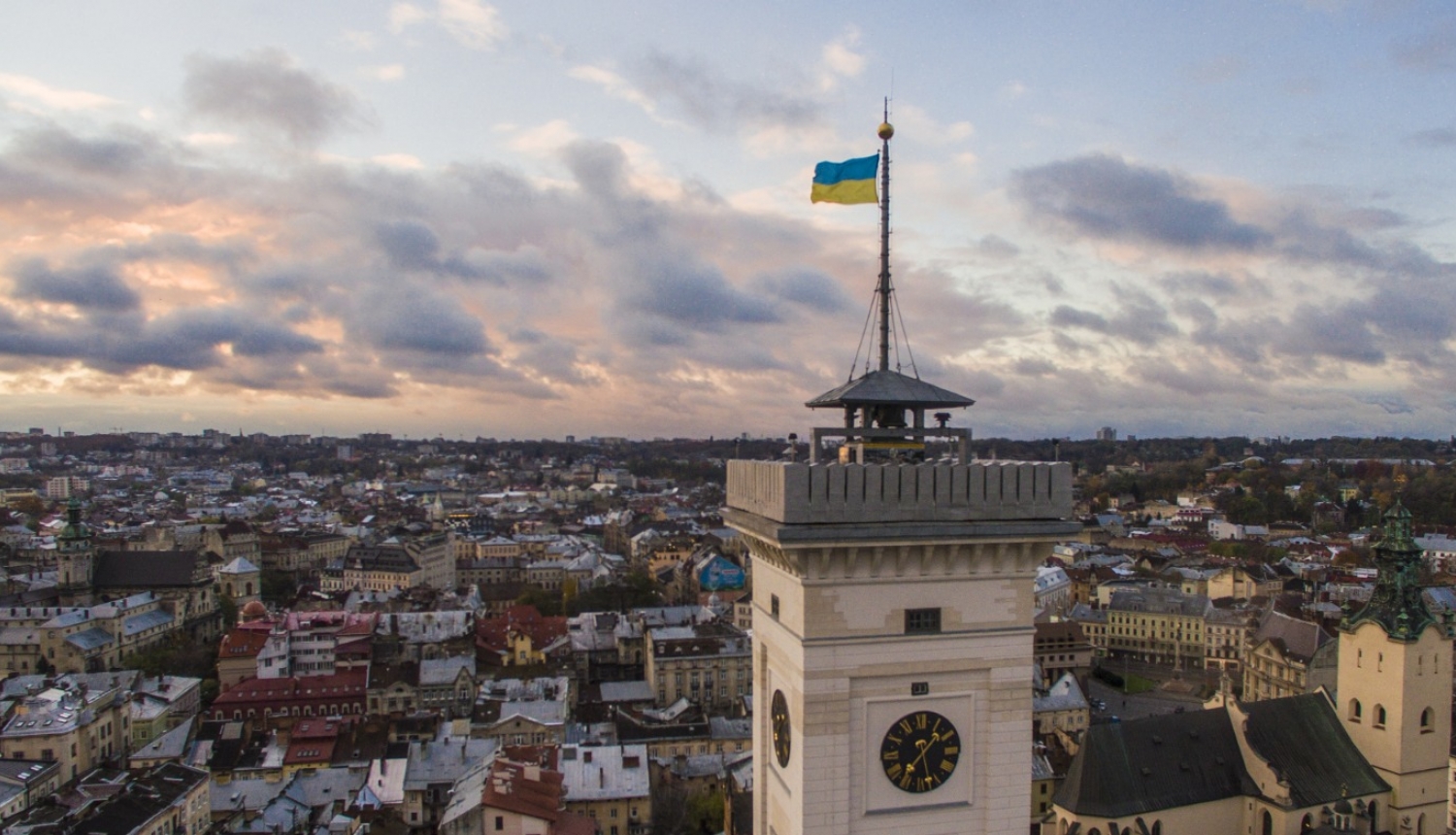 Skats no putna lidojumu pār Ukrainas pilsētu Ļvivu. Pirmajā plānā redzams pulksteņa tornis ar plīvojošu Ukrainas karogu